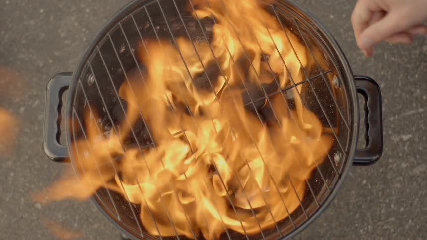 Person sets a grate on a flaming charcoal grill