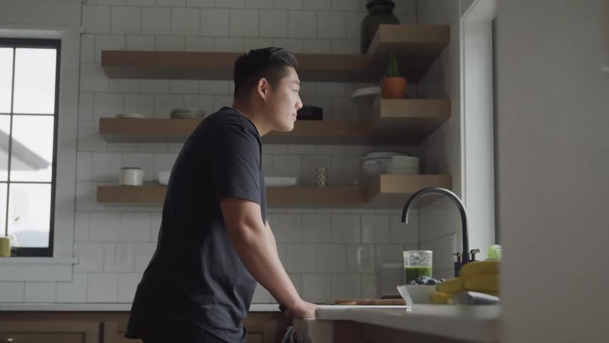 A man looks up contemplatively from the sink in the kitchen to look out the window