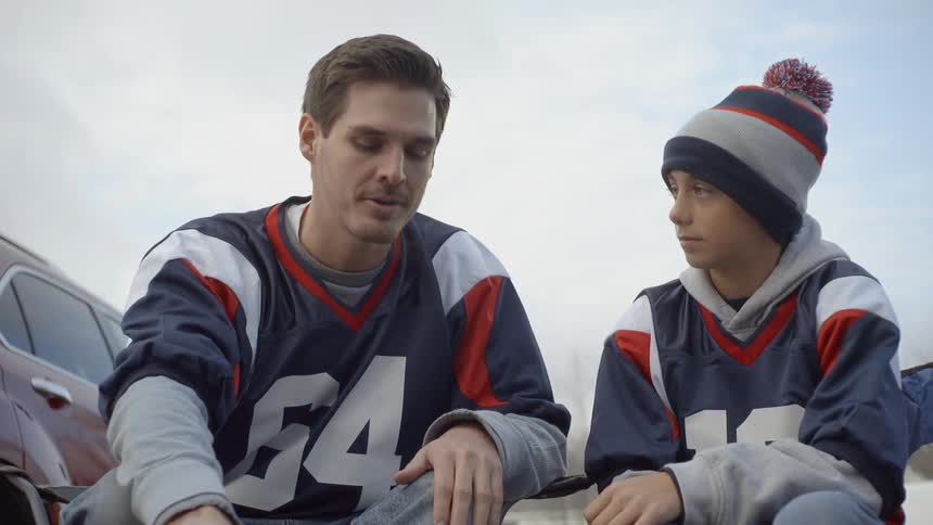 Man and boy dressed in football jerseys are sitting and talking outside on cold day