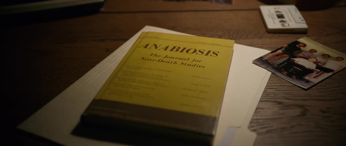 A book lays on a wooden desk next to a photograph and cassette