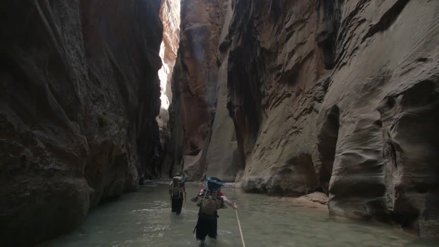 Two people walk through a river in a chasm