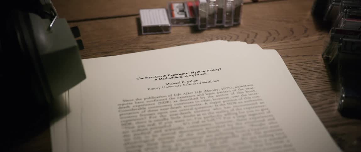 A stack of papers with printed text on them lay on a wood table surrounded buy cassettes