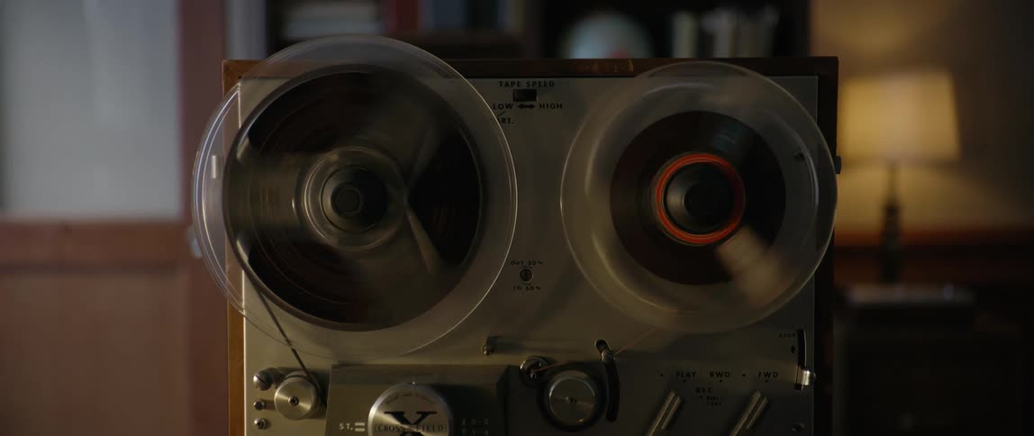 A vintage reeltoreel tape recorder is in operation with visible reels spinning and various control knobs and switches on the front panel