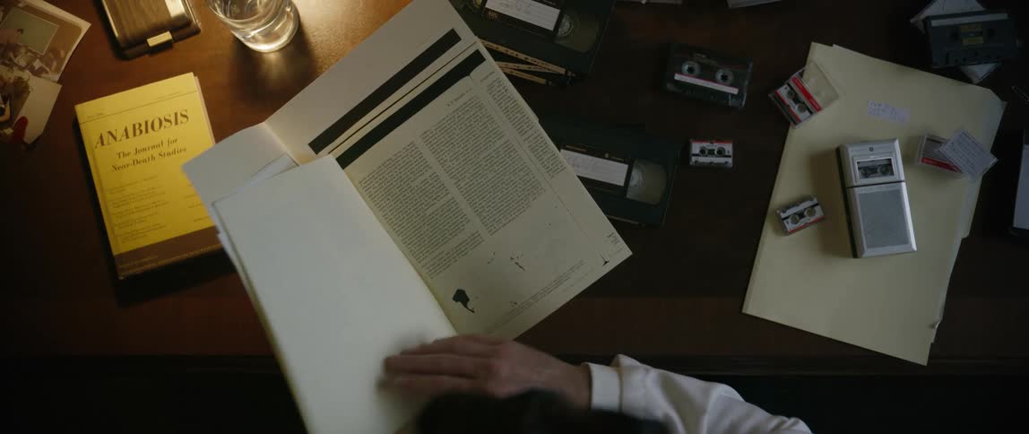 A man wearing a white shirt is reading some documents while sitting at a desk