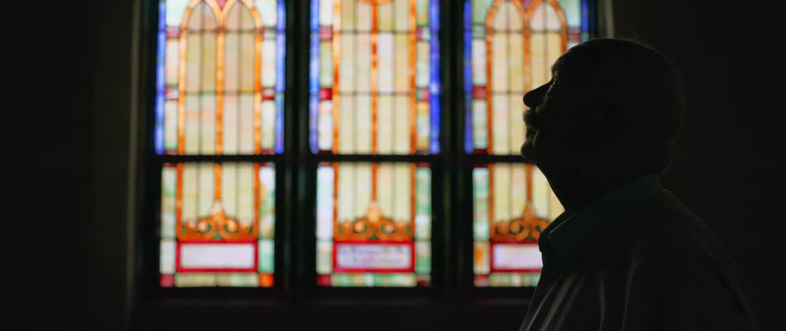 An older man in a church silently contemplating and praying