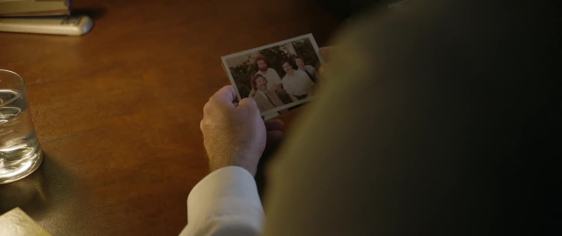 Man sitting at a wooden desk looks through photographs