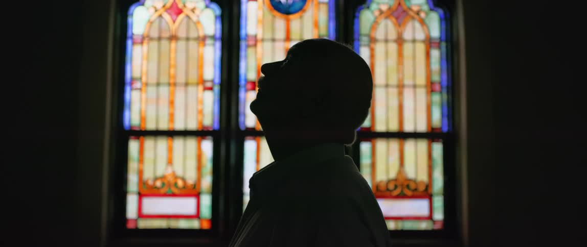 Silhouette of a man standing near a stained glass window inside a church