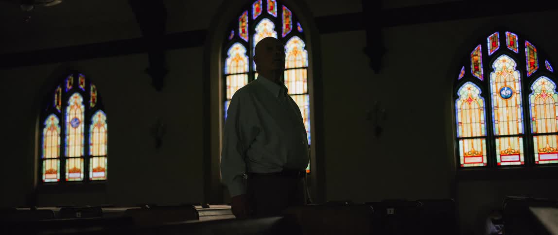 Silhouette of a man standing inside a dark church with stained glass windows
