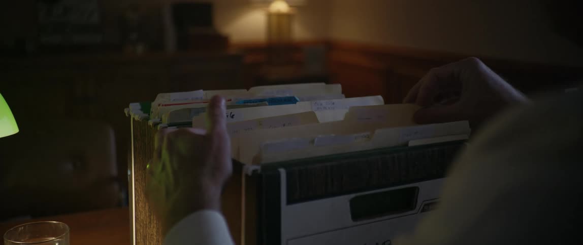 Man searching through files from a cardboard file box in a low lit office