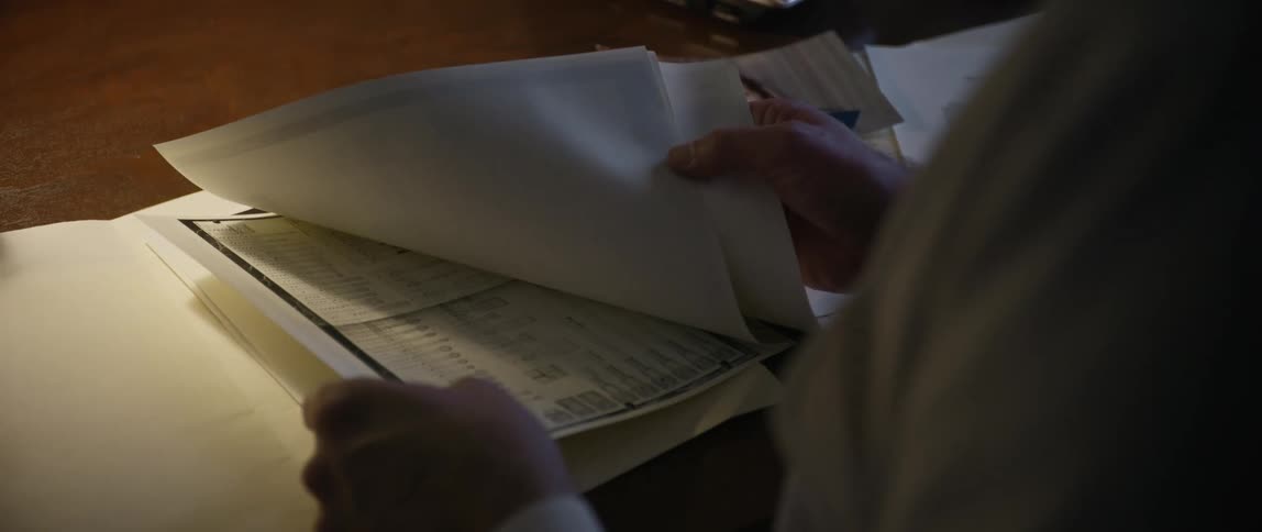 An elderly person flips through some papers in a file folder on a desk