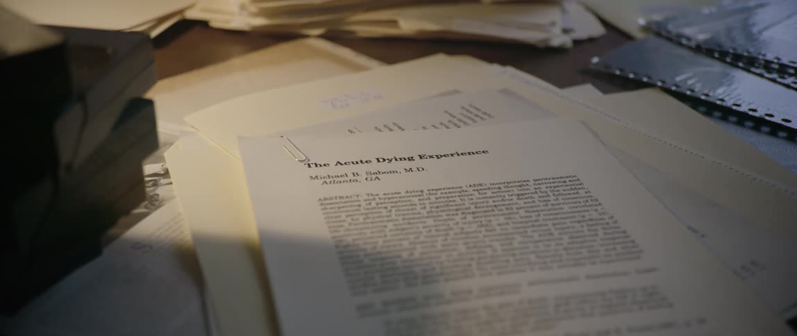 A paper titled the acute dying experiment sits on a desk amid other files and papers