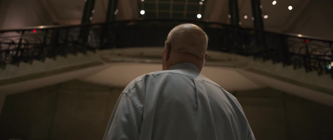 Elderly man walking through a building containing twin staircases looks around