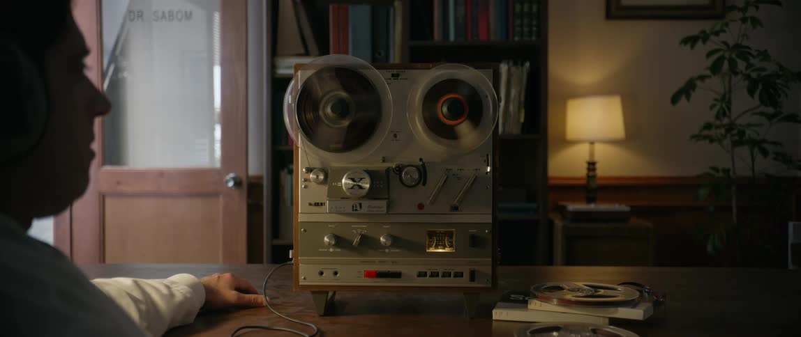 Man sitting at a dark table listens to recordings on an old reeltoreel tape recorder wearing headphones