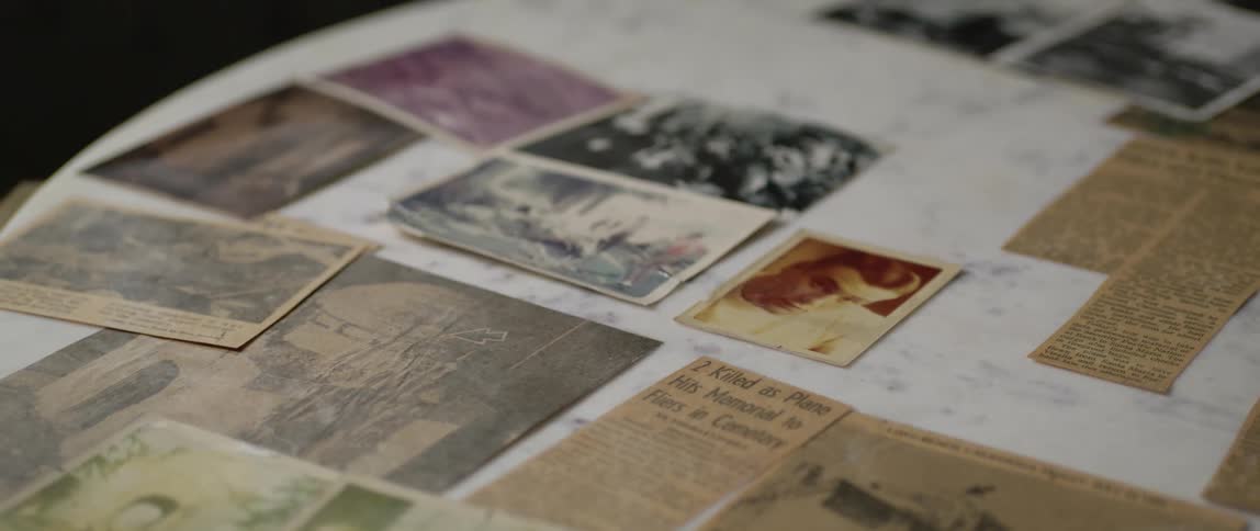 The camera pans over several pictures and newspaper articles that are laying on a table