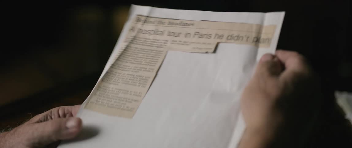 A man holding a piece of paper with a fragment of newspaper glued to it