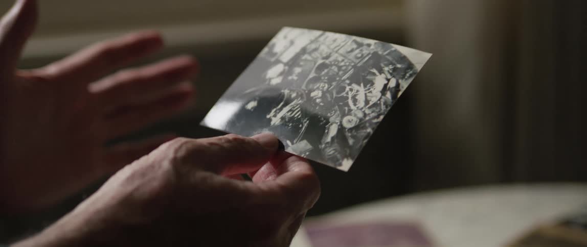 A persons hands are shown holding a black and white photograph depicting a cluttered scene
