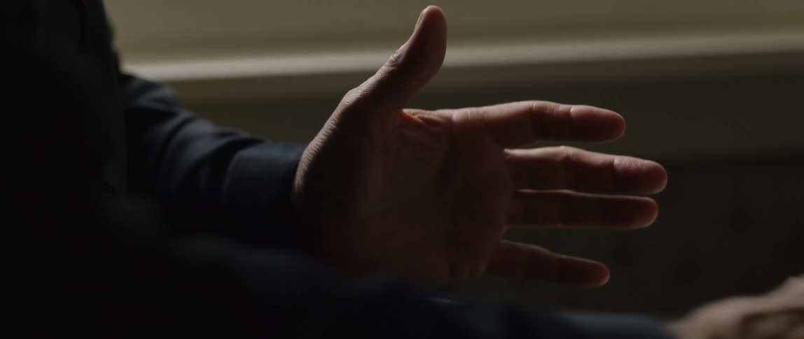 Closeup of a mans hands gesturing as he explains and picks up an object from a coffee table in dim lighting