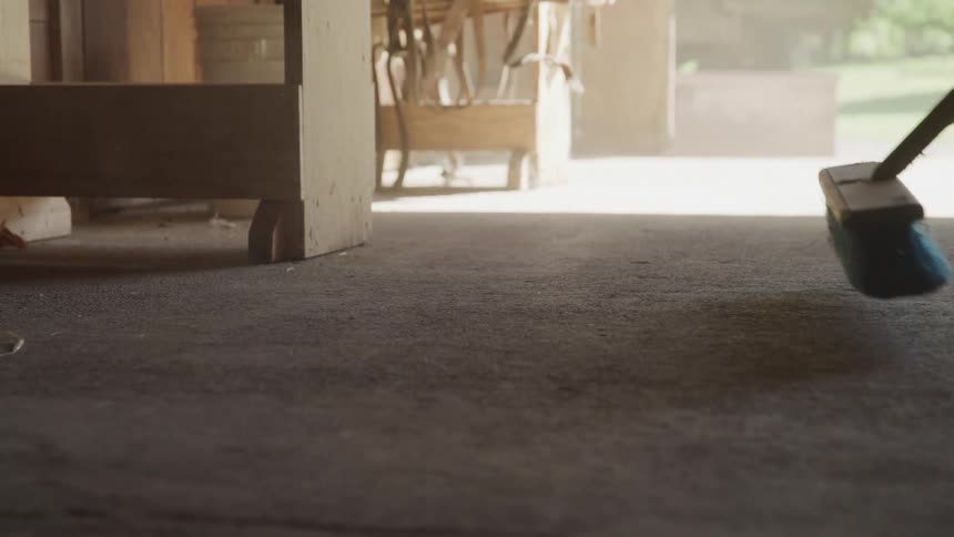 A person is sweeping out their garage during the day time