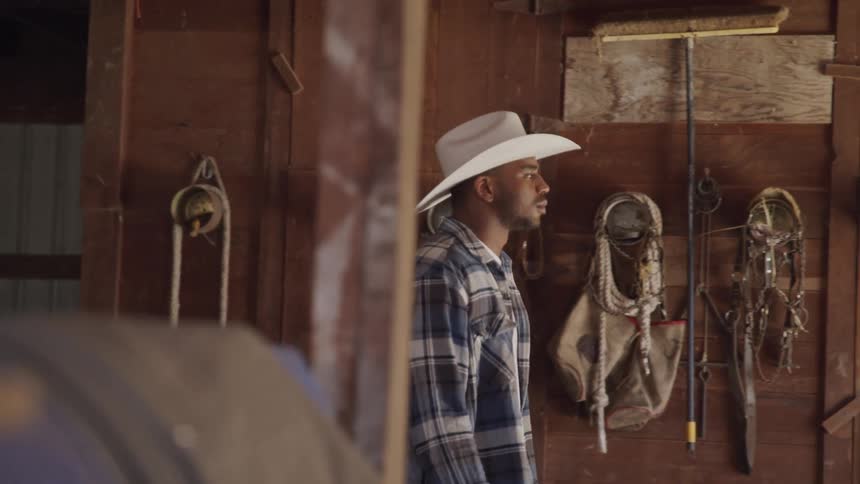 A man wearing a white cowboy hat is walking in front of a barn