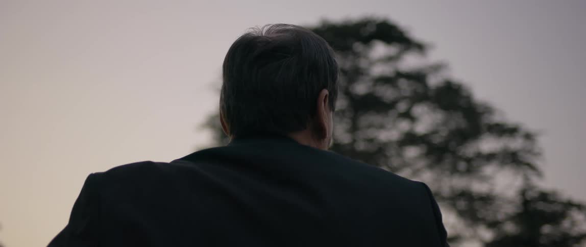 A man wearing a suit is pointing at a church at dusk