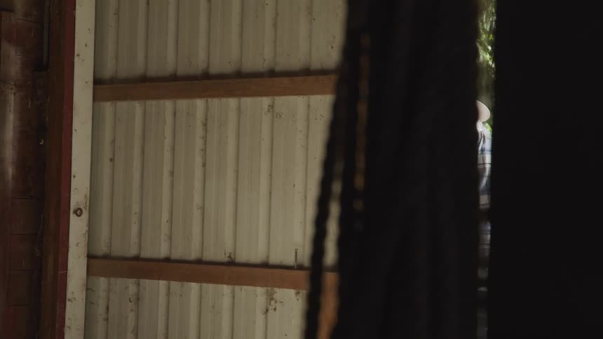 A man in a cowboy hat and plaid shirt opens the door to a barn or stable
