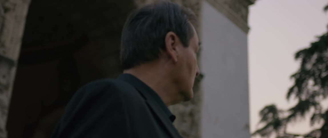 An elderly man wearing a suit is gazing at the cloudy sky near a temple