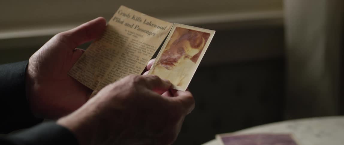 A man holds a small photo up to a clipping from a newspaper