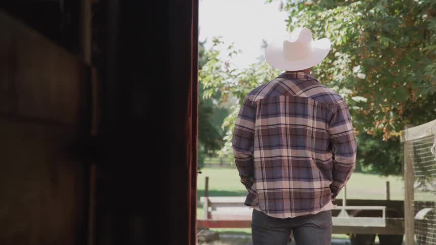 A cowboy is standing outside the barn