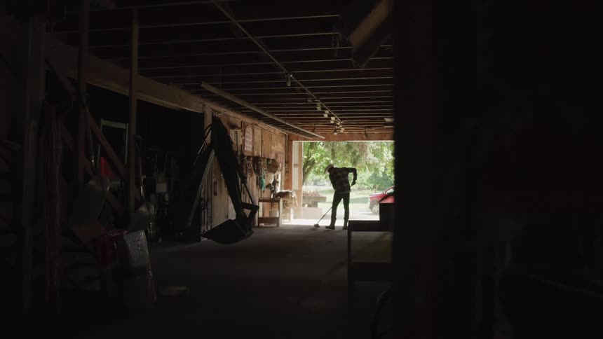 A man wearing a hat is sweeping the garage floor using a push broom
