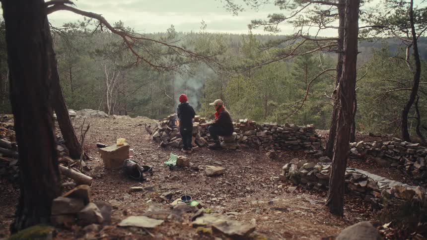 Father and son burning woods on a hill in a forest area at dawn