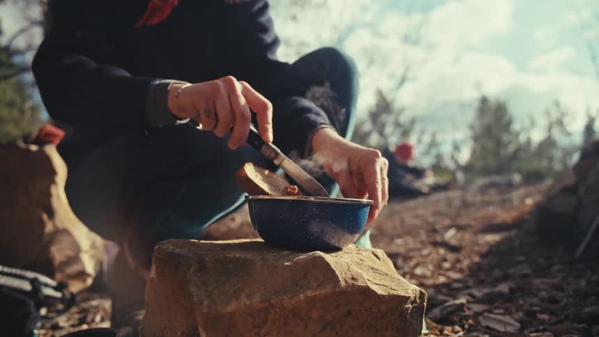 Person cutting thier morning breakfast in a bowl on a rock while camping