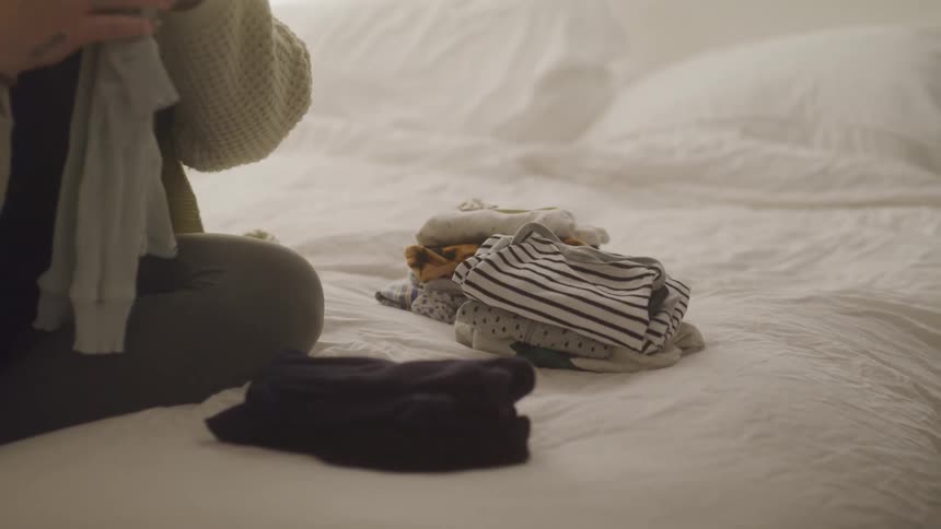 A woman is folding clothes on the bed
