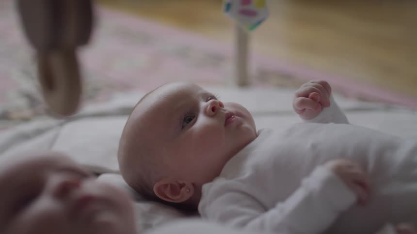 Infant twins laying on a blanket on the floor looking at toy hanging above