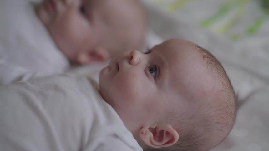 Closeup of a babys face in white clothes resting on a bed and looking upward