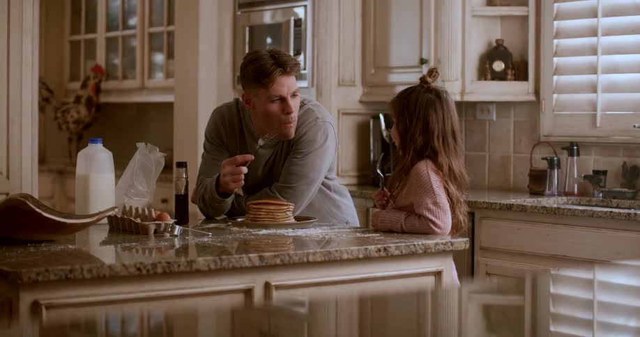 A father and daughter eat pancakes at the kitchen island
