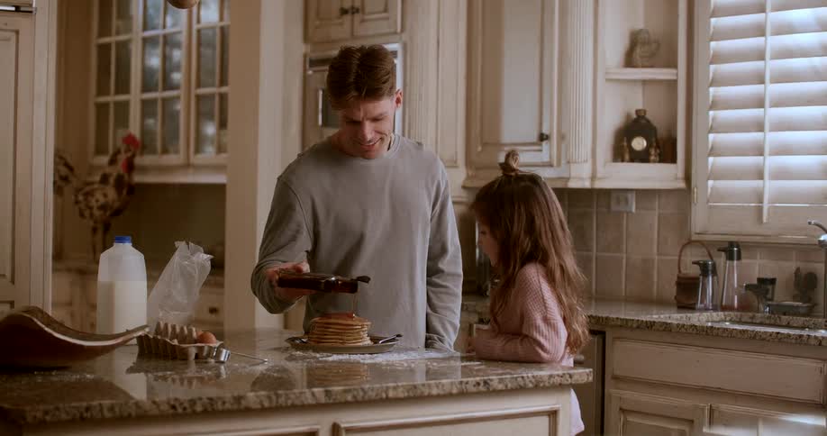 Father and daughter in the kitchen putting honey on a pancake
