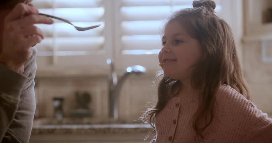 A father feeds his happy daughter pancakes