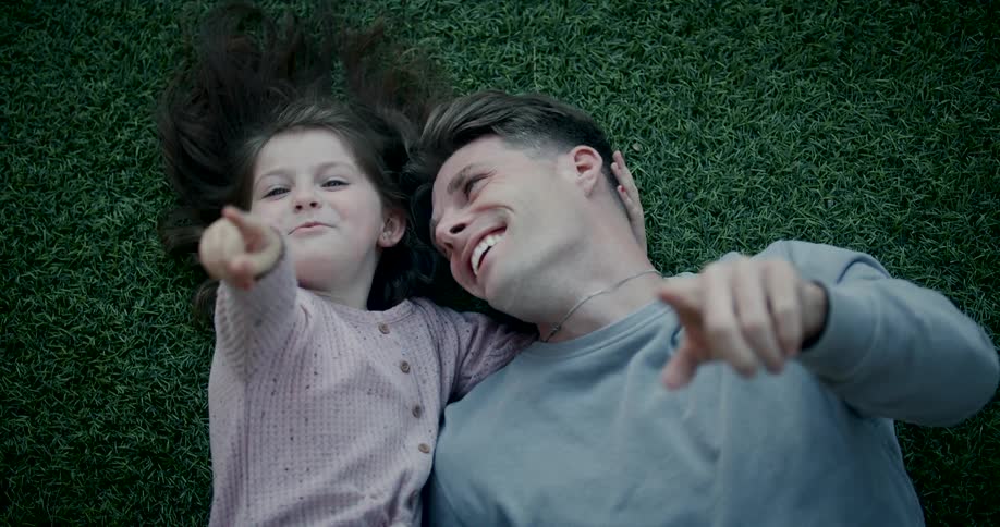 Cheerful father and daughter pointing finger up while lying on a green rug