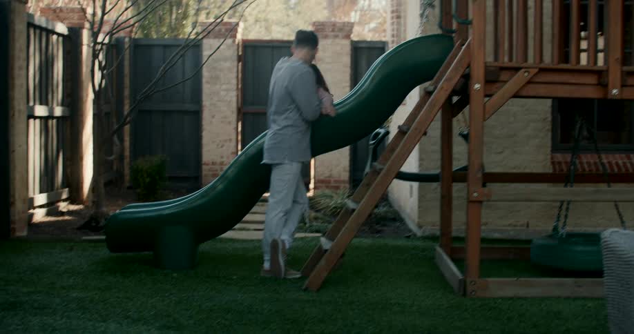 A father watches his daughter go down the slide