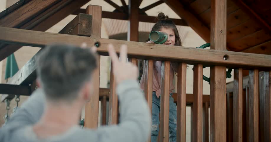 Young girl looking through telescope of playhouse as her dad wiggles two fingers from below