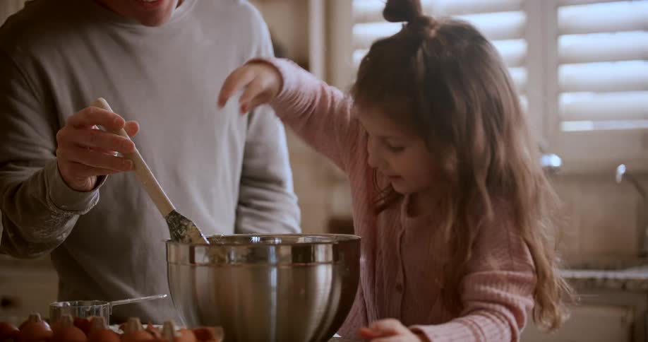 A father mixes as a girl cracks eggs into the bowl