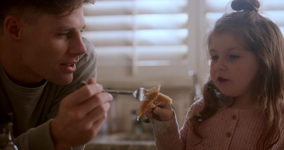 A father and daughter laugh while eating a stack of pancakes