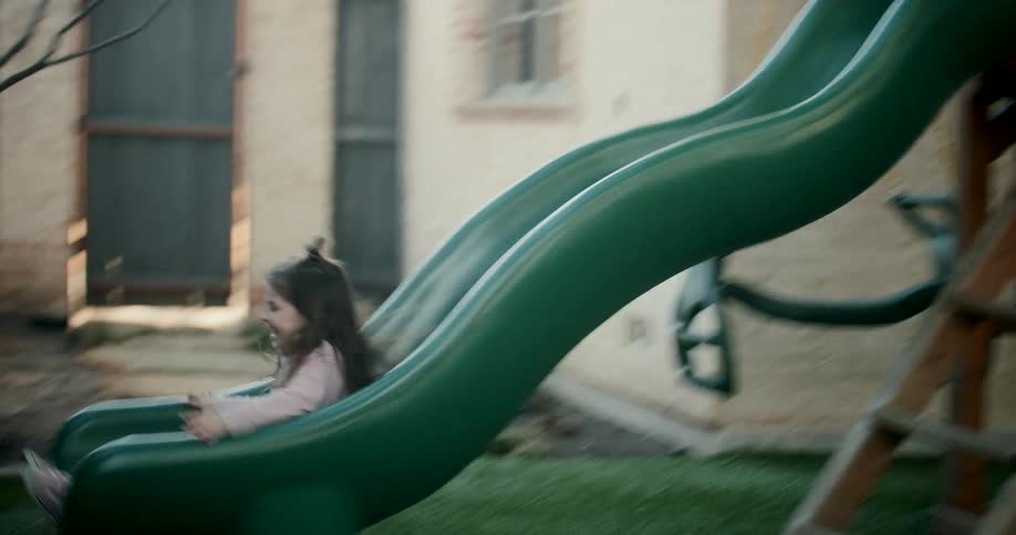 A girl slides in the playground and holds her fathers hand