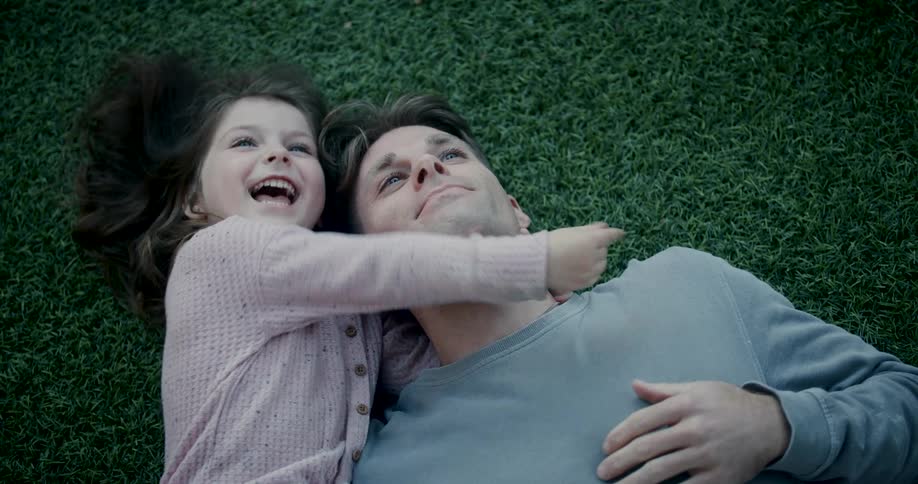 Father and daughter lying on the grass watching something in the sky