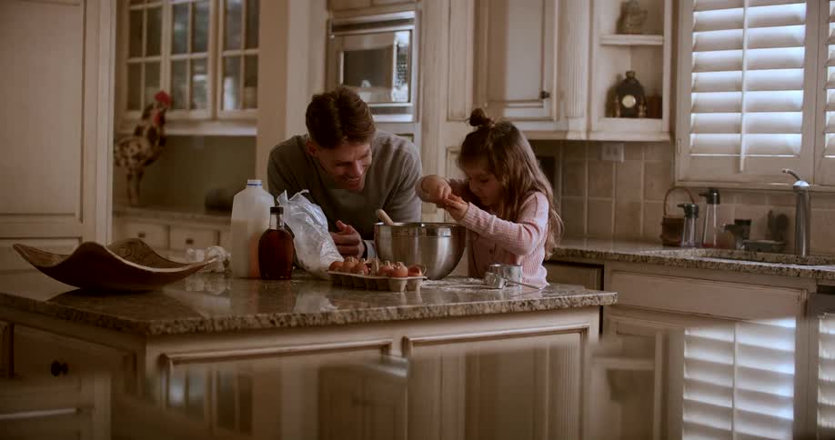 A girl is cooking with her dad in the kitchen