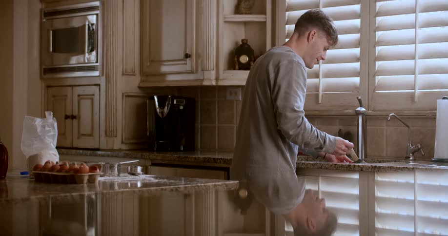 A man is standing by the kitchen sink and smiling while washing the dishes