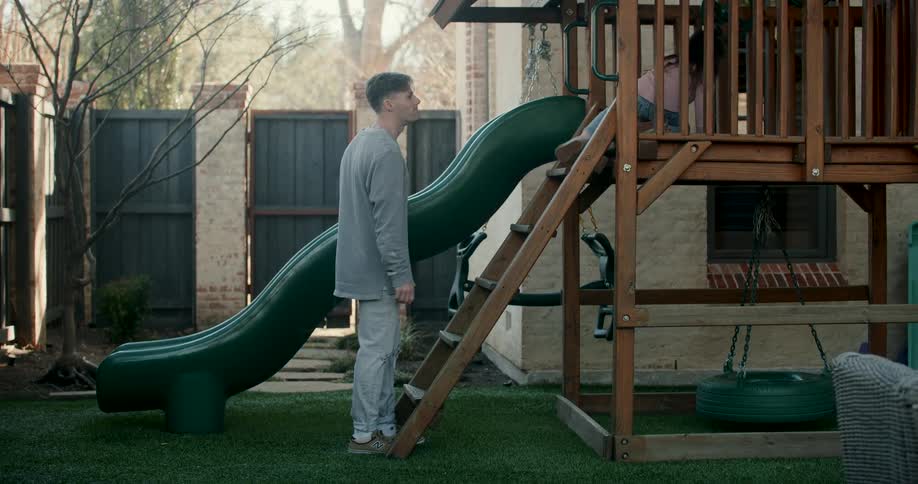 Father and daughter climb a ladder in a backyard playset on an autumn day
