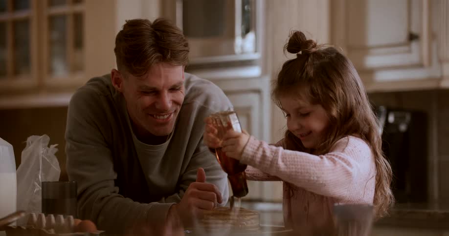 Father watching his daughter put honey in a pancake