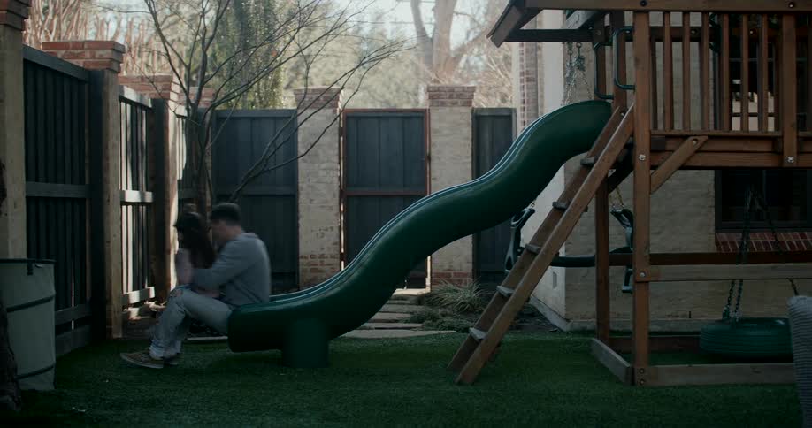 Father holds daughter as they both move down a curvy slide in a playground