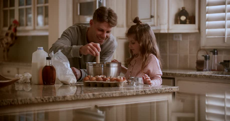 Father and daughter smile while mixing batter in their kitchen during the daytime